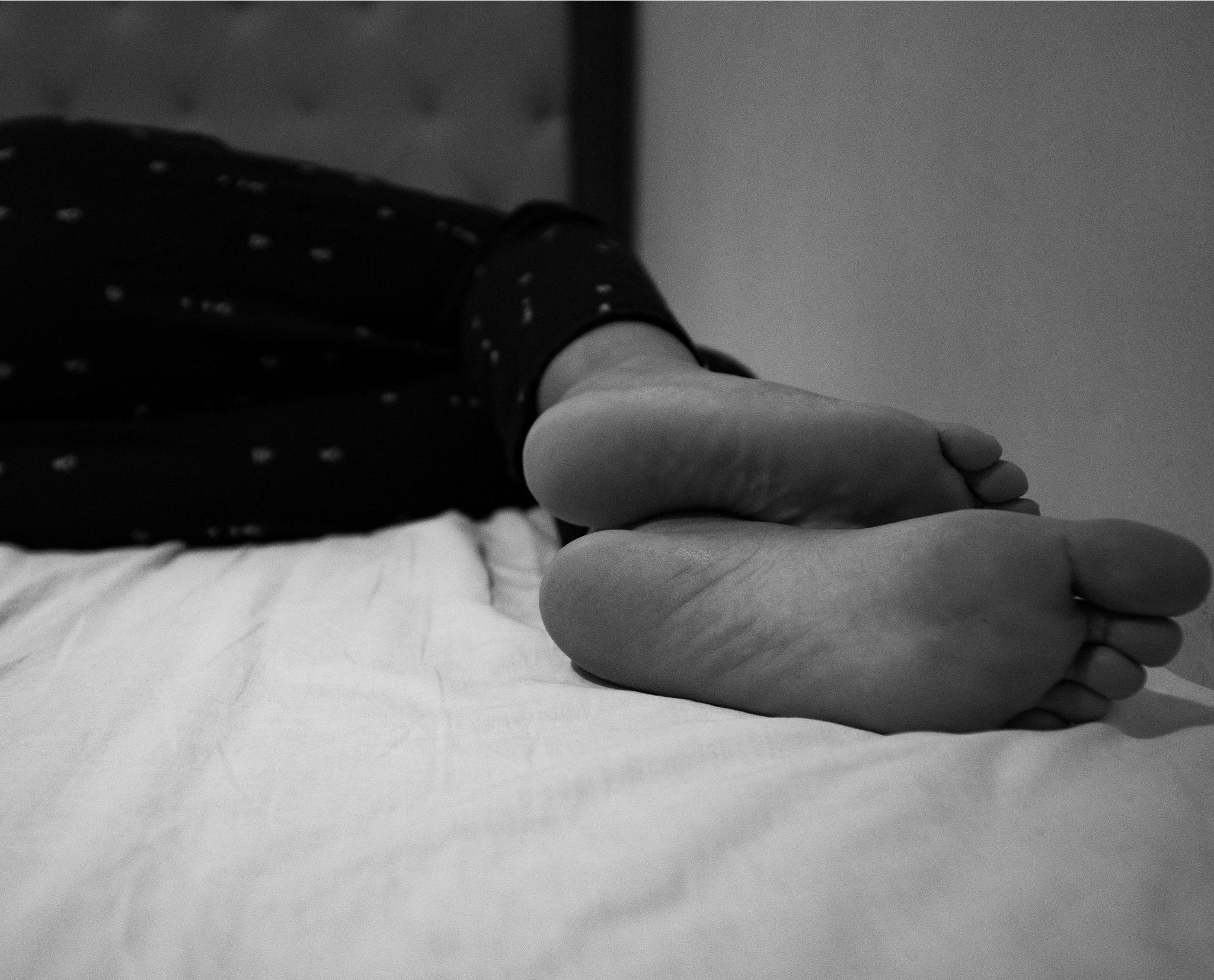 Une photo représentant des jambes et pieds d'une jeune femme couché sur un lit.  